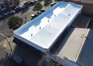 Aerial view of a commercial building with a newly installed white flat roof by Creative Roofs.