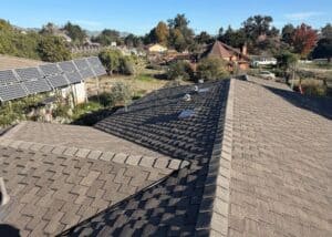 Newly installed architectural shingle roof on a residential home with solar panels in a suburban neighborhood.