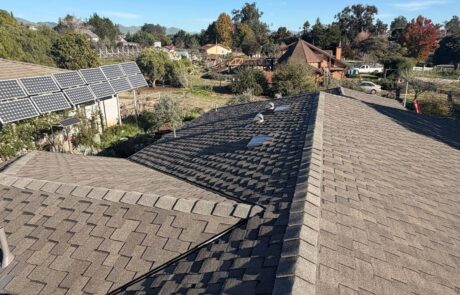 Newly installed architectural shingle roof on a residential home with solar panels in a suburban neighborhood.